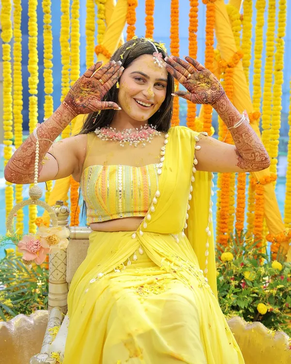 A joyful bride shows off her intricate henna designs during her Haldi ceremony. Her bright smile and the vibrant yellow decor create a picture of pure happiness and anticipation.