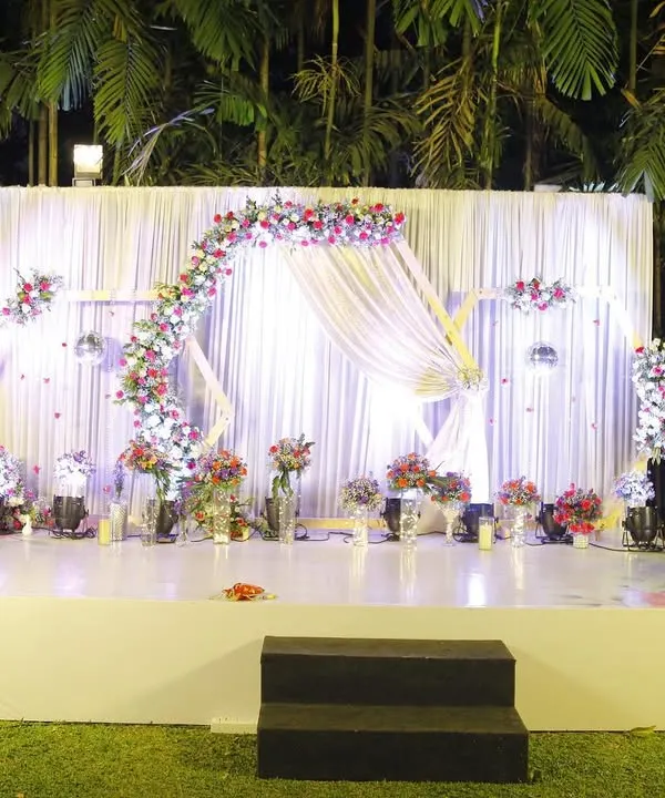 We designed this elegant reception stage for an intimate lawn wedding, creating a magical ambiance under the stars. The flowing white drapes, delicate floral arch, and soft lighting came together to produce a truly romantic setting for the couple's celebration.
