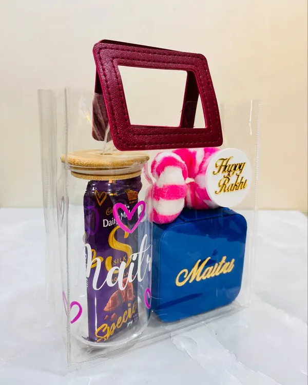 A special Rakhi hamper for a special sister. This one comes in a clear tote bag and includes a customized glass tumbler, a personalized jewelry box, a scrunchie, and her favorite chocolate.