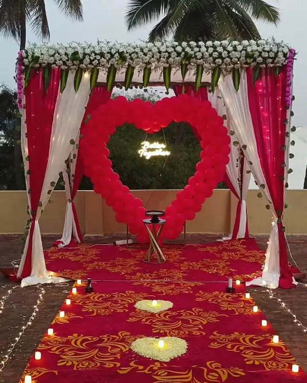 A perfect proposal setup on a rooftop, complete with a red carpet, candle-lit pathway, and a large heart-shaped balloon arch framing a 'Better Together' neon sign.