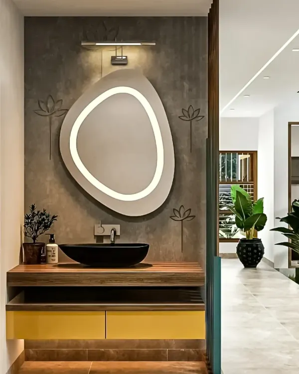 A chic washbasin area featuring a unique, organically shaped backlit mirror. The floating wooden vanity with a black vessel sink and yellow drawers adds a pop of color and modern flair.