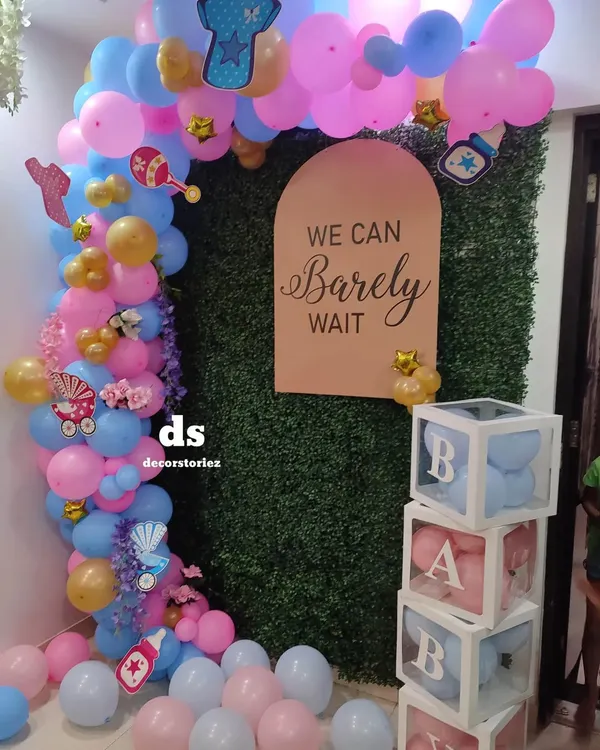 Here is a popular baby shower theme we created, perfect for a gender reveal. The setup includes a pink and blue balloon arch against a green wall, a custom "We Can Barely Wait" sign, and transparent 'BABY' blocks filled with matching balloons.