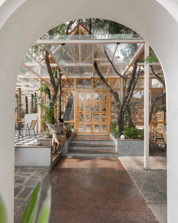 The entrance to the Bake House, framed by a traditional archway. The view reveals a glass-and-wood pavilion built carefully around existing trees, immediately establishing the project's nature-centric theme.