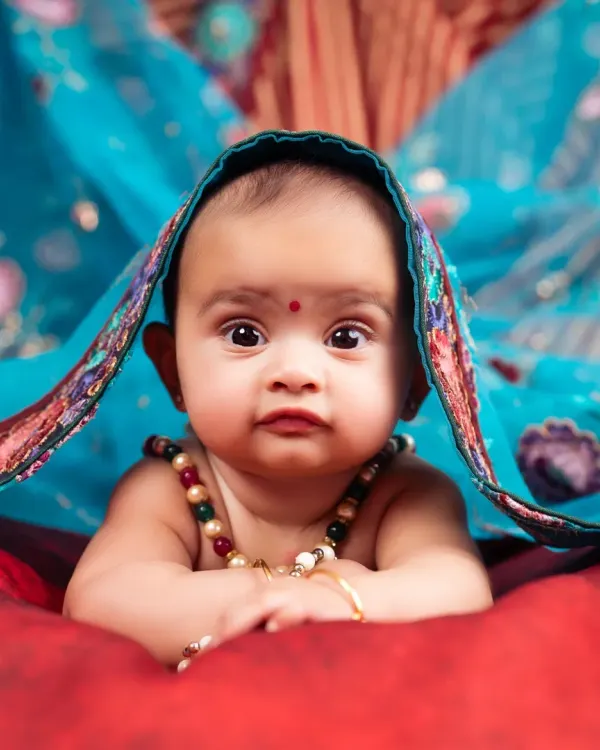 A stunning close-up of a 6-month-old baby, peeking from under a vibrant blue dupatta. A beautiful blend of tradition and cuteness.