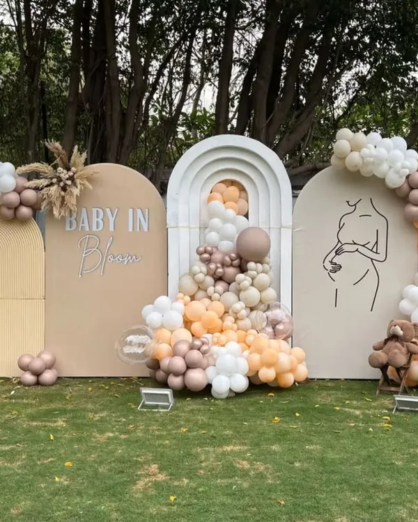 A beautiful outdoor "Baby in Bloom" baby shower setup, perfect for a modern celebration. This design features trendy neutral and blush-toned balloon garlands on triple-arched backdrops, creating an elegant and sophisticated photo corner.