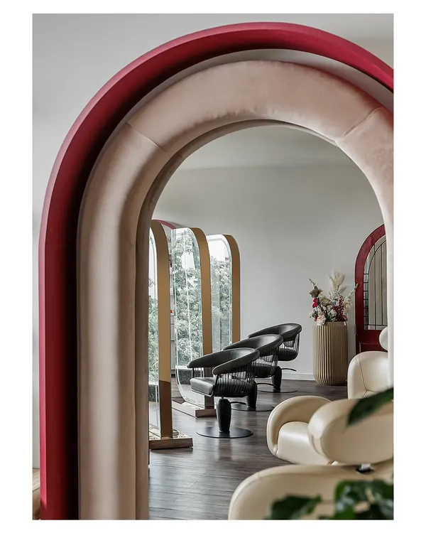 A view through a series of plush, velvet-lined arches reveals the salon's styling stations. This architectural feature creates a sense of drama and discovery, guiding clients through the space while offering glimpses of what lies beyond.