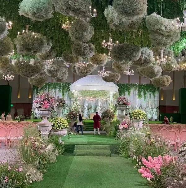 A breathtaking view of an Italian garden-themed wedding, with a lush green aisle leading to a domed mandap. The ceiling is a cloud of baby's breath and chandeliers, creating a truly magical atmosphere.