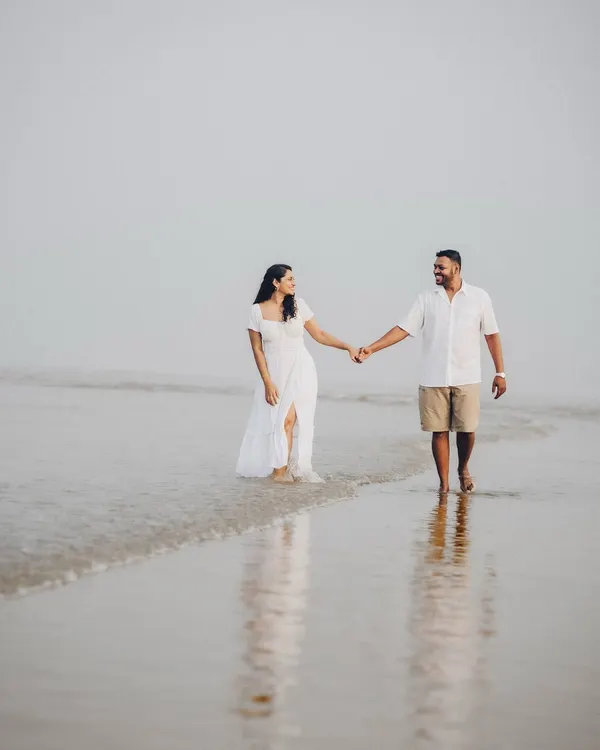 Janice and Lyle walking hand-in-hand during their misty morning beach session. The soft light and reflections on the wet sand create a dreamy, ethereal quality.