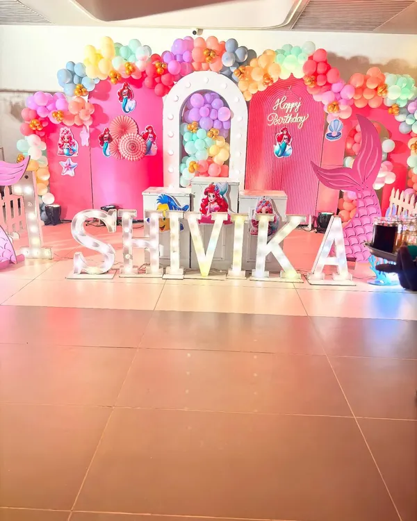 This is a complete stage setup for a Little Mermaid theme party. I used a vibrant pink backdrop, a colorful balloon arch, and large marquee letters, along with multiple cutouts of Ariel and her friends to create a lively underwater scene.