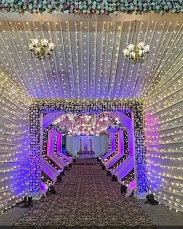 This illuminated tunnel is one of my signature entrance designs. The combination of fairy lights, draped fabric, and floral details creates a grand and magical pathway for your guests.