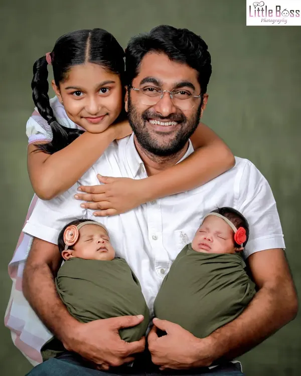 A proud father with his three children, holding his newborn twins while his older daughter gives him a hug. A heartwarming studio portrait of a growing family.