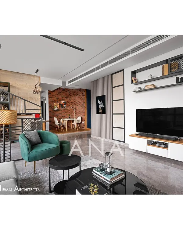 The living area of Apartment 704, designed for a retired couple with a fondness for minimal design. The space combines a neutral grey palette with a pop of green, raw brick textures, and a custom metal partition to create a layered, contemporary feel.