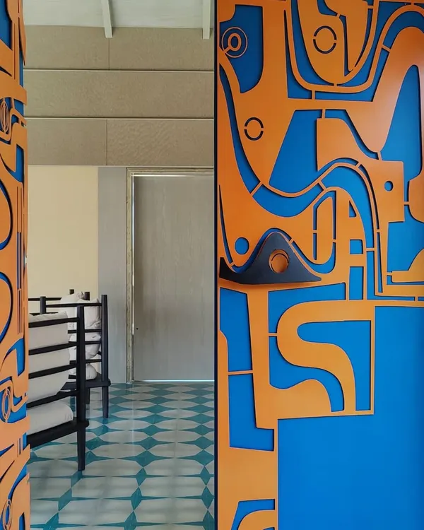 A close-up view of our custom-designed metal door, showcasing the layered mild steel construction and the unique, hand-sculpted handles. The vibrant contrast between the orange and blue creates a powerful visual impact.