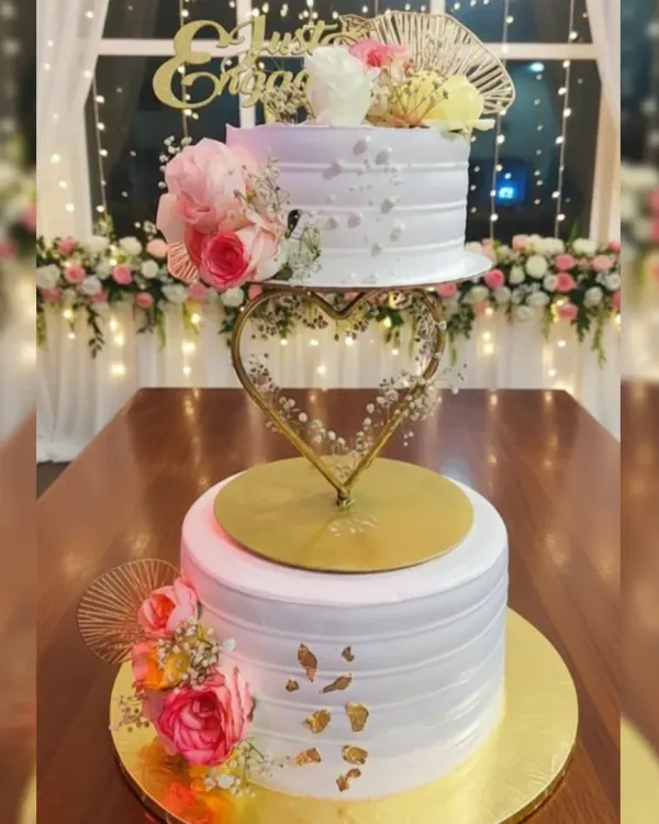 I love how a spacer can add so much elegance to a tiered cake. This two-tier engagement cake features a heart-shaped spacer, fresh florals, and gold leaf accents on a delicious eggless pineapple cake.