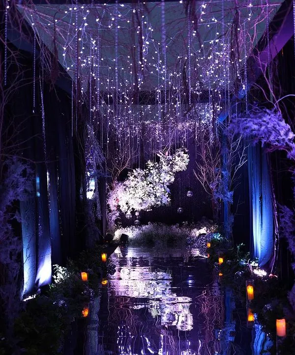 An ethereal entrance for an enchanted forest themed party. We used a reflective floor, cascading fairy lights, and purple uplighting on bare branches to create this magical, otherworldly atmosphere.