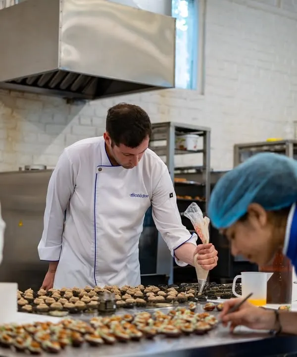 Here is Chef Maxime Montay leading his team in the kitchen. This behind-the-scenes shot shows the focus and collaboration that goes into preparing for a large event.