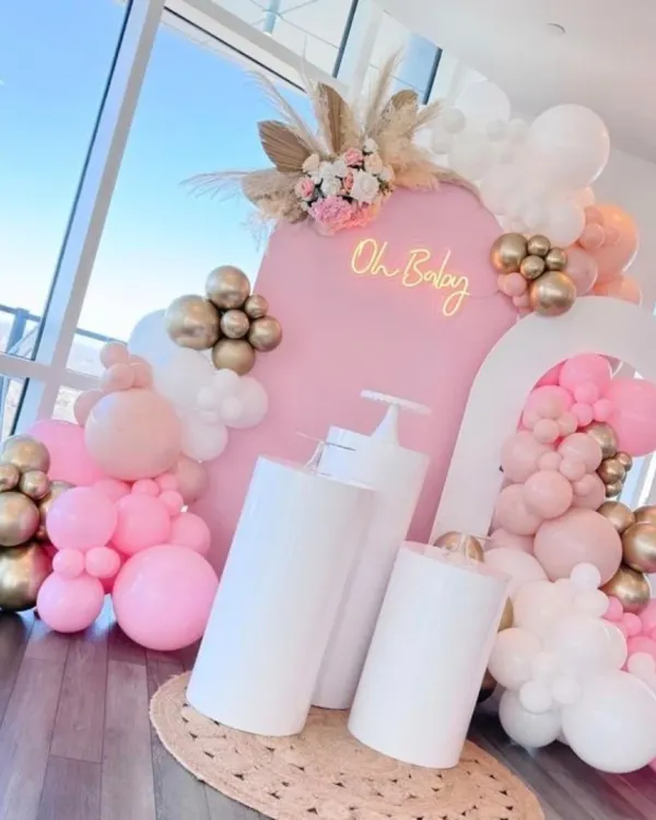 A chic and modern baby shower setup with a pink arched backdrop, an 'Oh Baby' neon sign, and a beautiful balloon arrangement in pink, white, and gold. The pampas grass and floral accents add a touch of boho elegance.