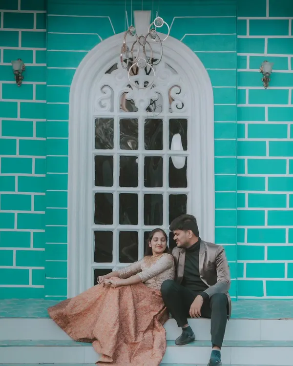 A romantic moment on the steps of a building with a beautiful turquoise brick wall. The bride's flowing gown and the elegant setting create a modern fairytale look.