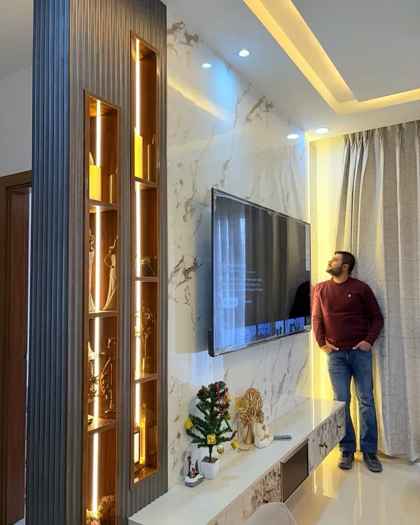 Admiring a finished TV unit. This design features a marble-finish back panel, a fluted wood partition with illuminated display niches, and a sleek console, creating a stunning centerpiece for the living room.