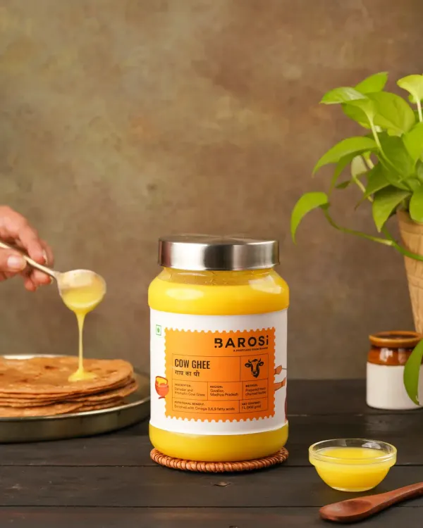 A lifestyle shot showing A2 Cow Ghee being drizzled onto a stack of parathas. This image demonstrates the product in use, making it instantly relatable and desirable for a home kitchen.