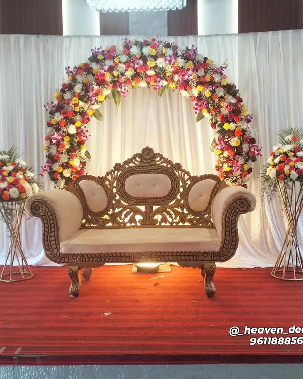 A classic and beautiful full floral arch provides a timeless backdrop for any reception or engagement. The mix of colorful flowers creates a vibrant and celebratory focal point, complemented by an ornate, traditional sofa.