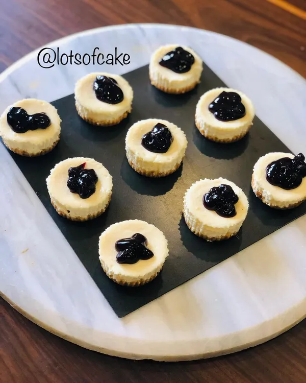 An aerial view of my mini blueberry cheesecakes arranged on a platter. Each one is a perfect, creamy bite with a dollop of blueberry topping.