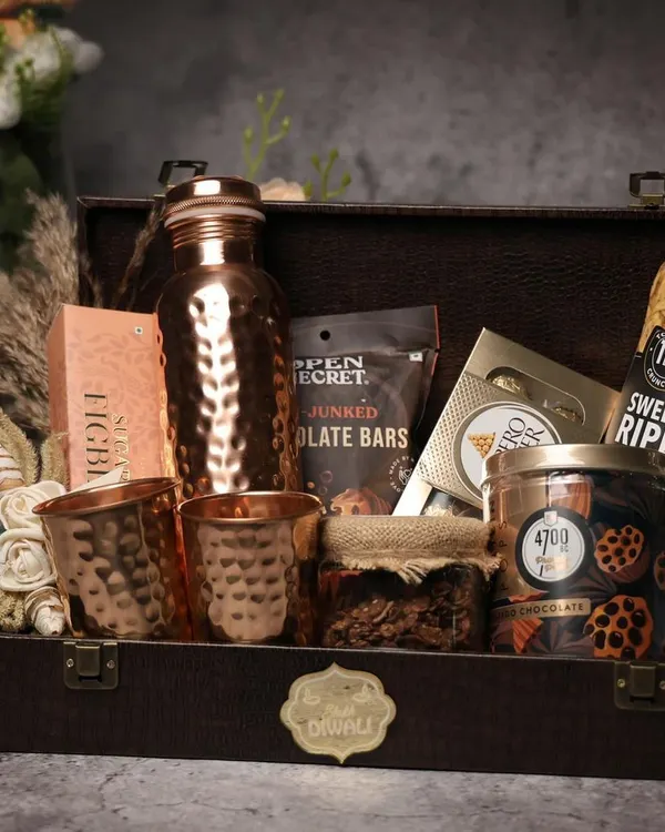 A classic Diwali hamper featuring a hammered copper bottle and glasses, packed in a rustic leather-finish trunk. This gift combines traditional wellness with modern aesthetics, filled with gourmet snacks and treats.