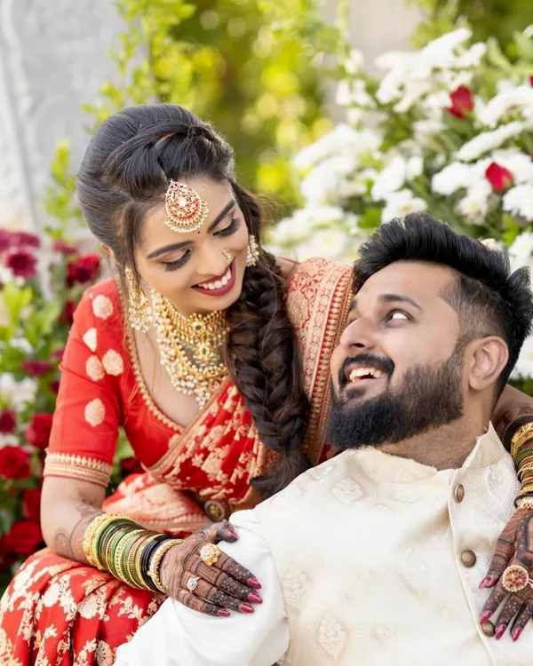 A candid moment of joy between the bride and groom. Her deep red saree and gold jewelry are beautifully accented by the rich color of her full-hand bridal mehendi.
