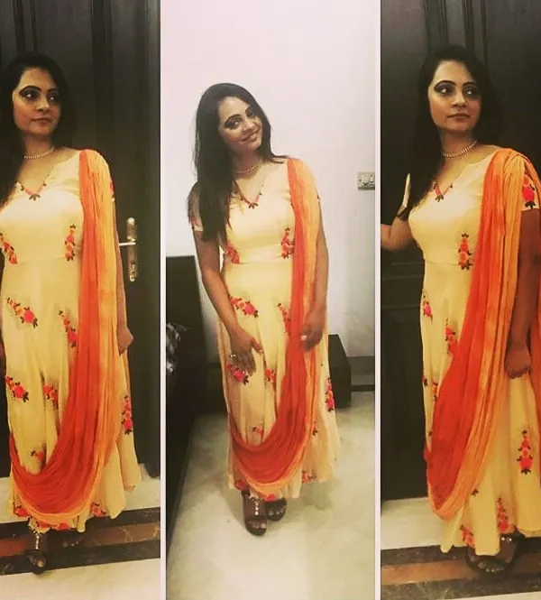 A client looking lovely in a custom-designed floral Anarkali. The light peach fabric is complemented by a contrasting orange dupatta, making it a graceful and comfortable choice for a daytime event.