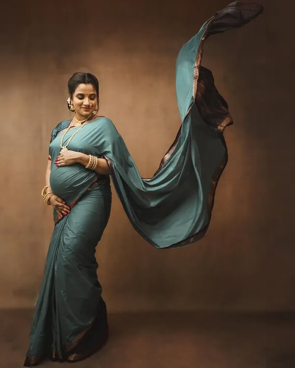 An artistic maternity portrait capturing the beauty and grace of motherhood, with the flowing fabric of the saree adding a sense of dynamic elegance.