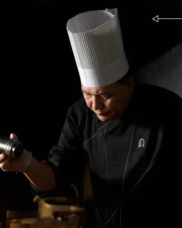 Sharp instincts and sharp skills. Our head chef is captured in a moment of intense focus, adding the final seasoning to a dish before it leaves the kitchen.
