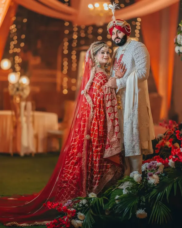 Gurneet and Gurbani in a classic Sikh wedding portrait. The bride's red dupatta and the groom's white sherwani create a stunning contrast against the warm, festive lights.