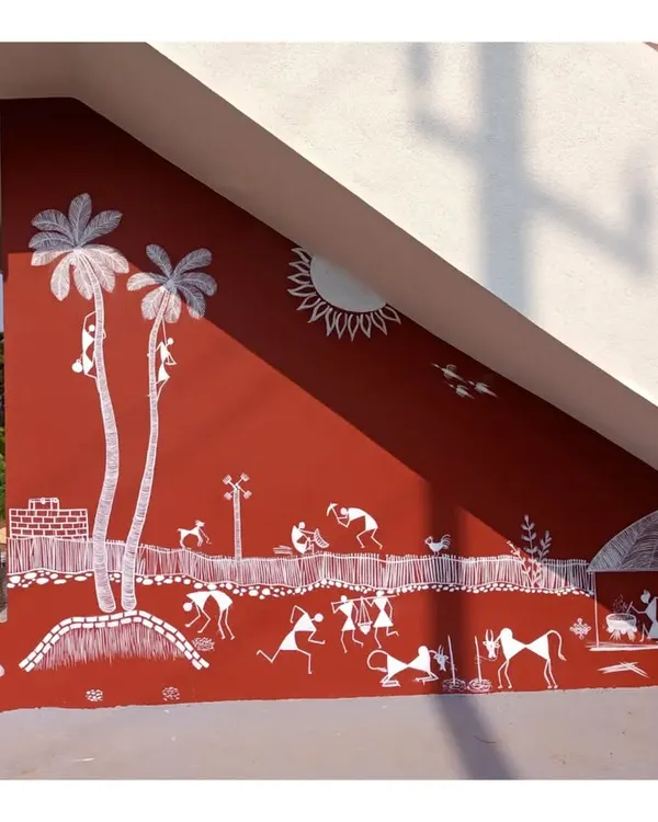 This wide-angle shot shows the full scale of a Warli mural I painted under a staircase. The composition fills the entire angled wall, depicting a lively village scene with palm trees, animals, and people engaged in various activities.