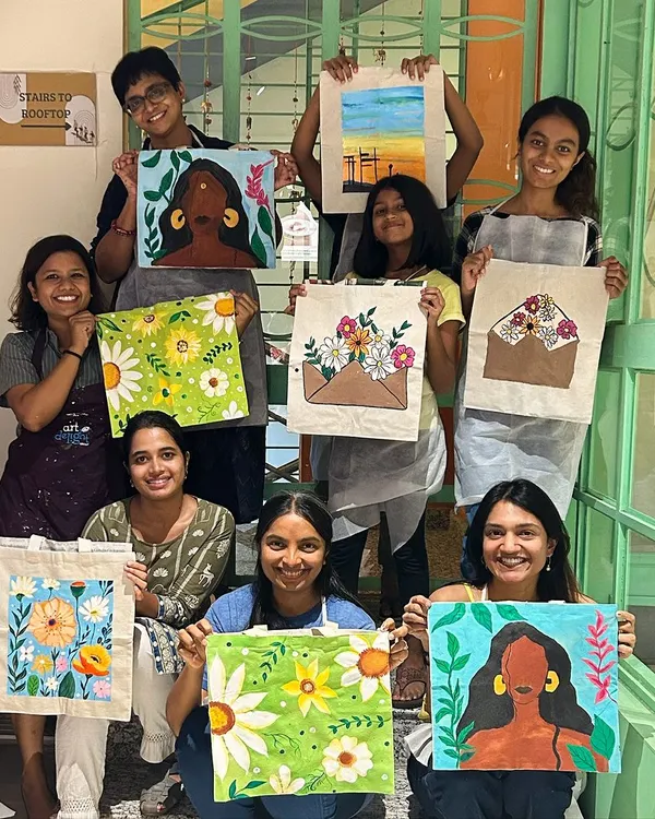 A group of happy artists showing off their custom-painted tote bags. From floral designs to abstract portraits, each bag is a unique expression of their creativity.