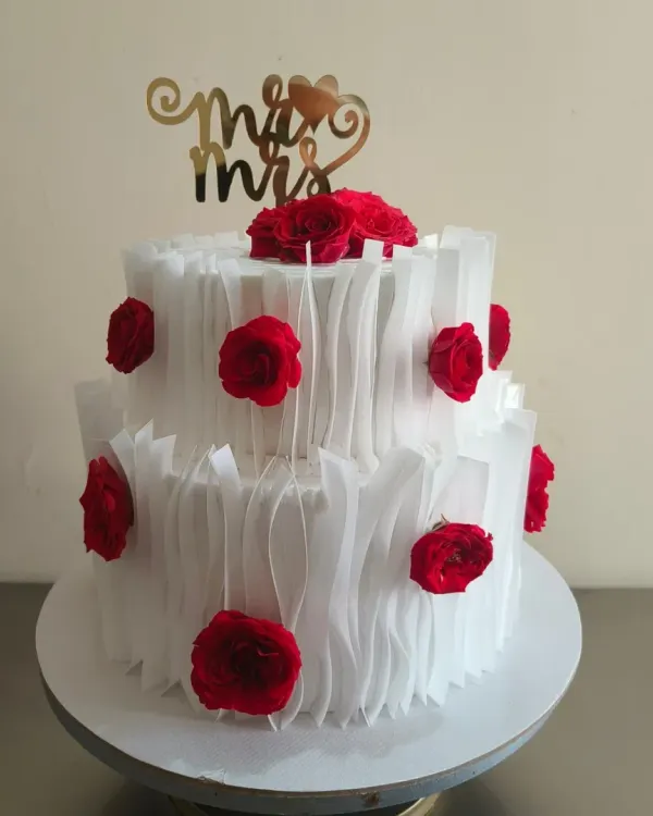 A beautiful two-tier wedding reception cake with a modern wafer paper ruffle design and vibrant red roses. The "Mr & Mrs" topper adds the perfect finishing touch.