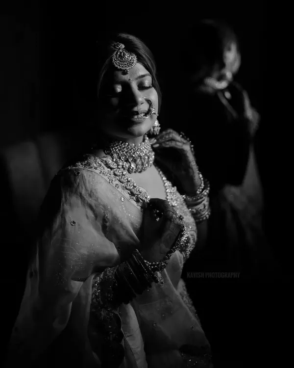 An artistic black and white bridal portrait, using dramatic low-key lighting to highlight the bride's jewelry and serene expression.