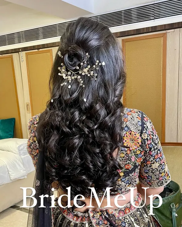 A beautiful half-up, half-down hairstyle for a reception. This style features a delicate rose made of hair and a sparkling accessory, with the rest of the hair in soft, bouncy curls.