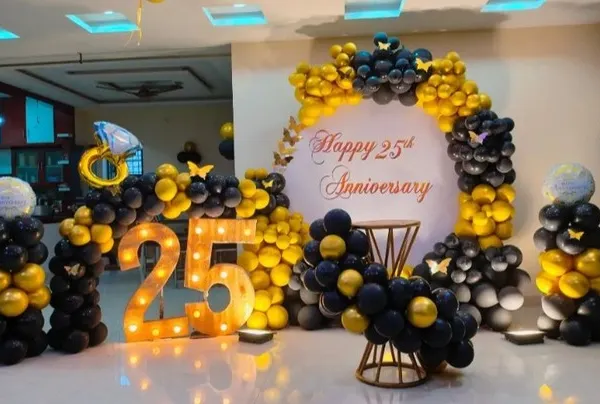 A grand 25th anniversary celebration featuring a striking black and yellow balloon arch, matching balloon pillars, and large marquee numbers. The color scheme is bold and celebratory, perfect for a major milestone.