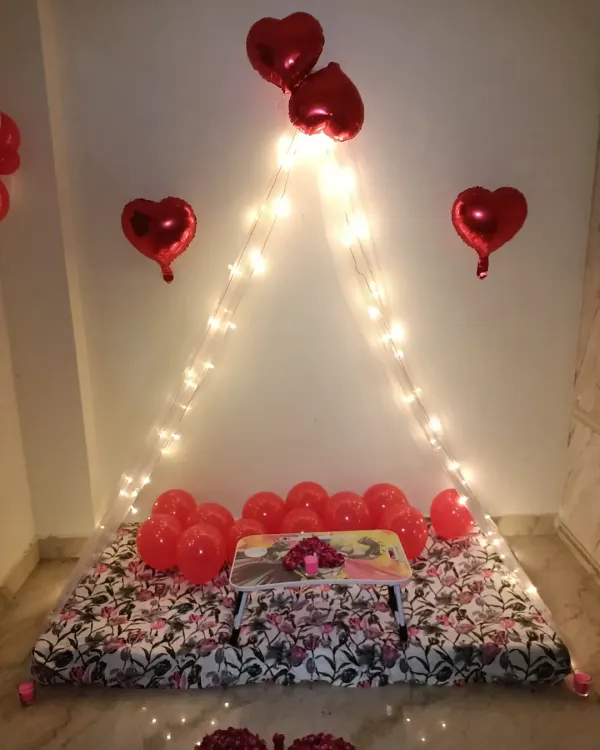 A great example of my simple and affordable cabana decor. This setup for a sixth-month anniversary uses a floor mattress, a fairy light canopy, and red heart-shaped foil balloons for a classic romantic look.