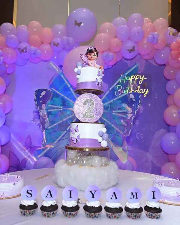 A stunning butterfly-themed birthday party setup, featuring our three-tier cake with a fairy topper and matching name cupcakes for "SAIYAMI".