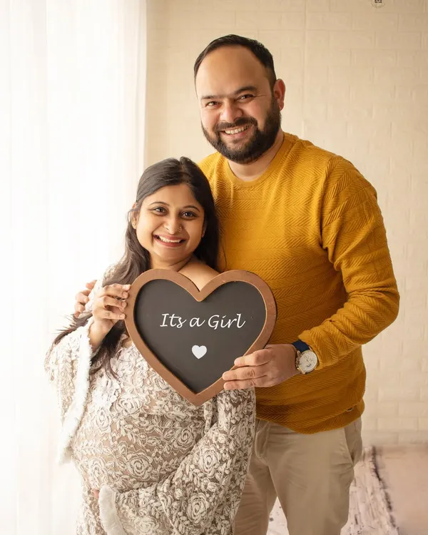 A happy couple announcing "It's a Girl" with a heart-shaped chalkboard sign. A simple and sweet way to share your exciting news.