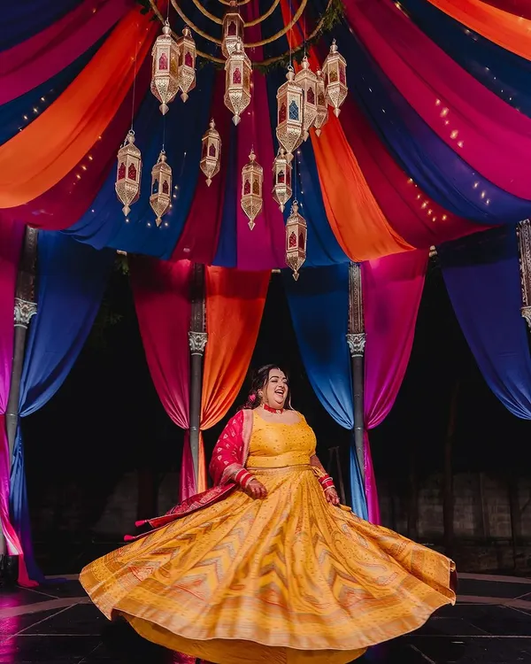 A bride twirls in her vibrant yellow lehenga during her Sangeet, set against a spectacular Moroccan-themed backdrop with colorful drapes and hanging lanterns. This is how I bring a theme to life with energy and style.
