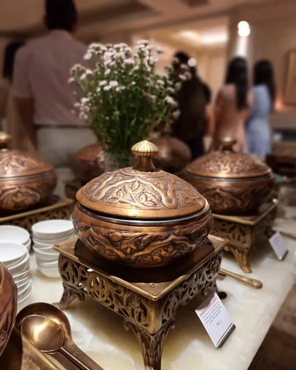 Our signature Mughlai dinner setup, featuring intricately carved copper and brass serving dishes. This presentation style is essential to the authentic, high-end Indian dining experience we provide for weddings and special occasions.