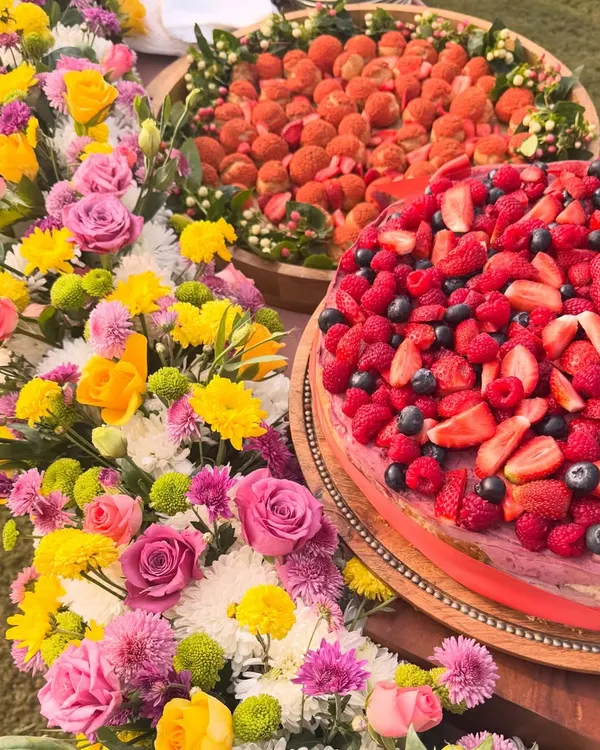 A beautiful dessert table I created for a family gathering. It features a large berry-topped cheesecake and a platter of our strawberry choux pastries, surrounded by fresh flowers.