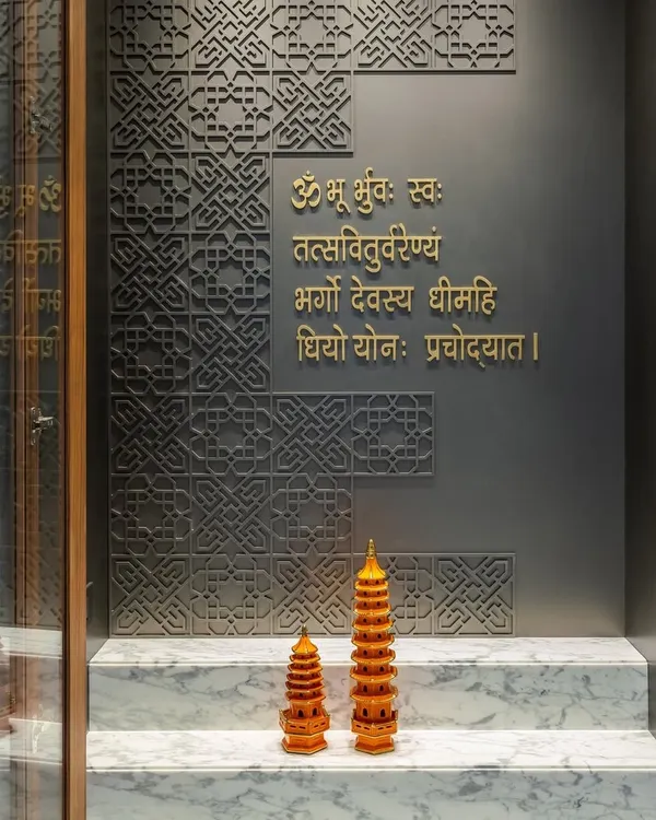 For this mandir design, we used a dark gray backdrop with intricate geometric carvings and the Gayatri Mantra in elegant gold lettering. The design is simple, sustainable, and creates an air of mystique.