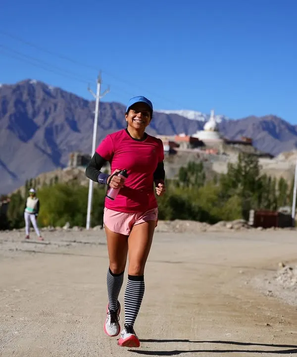 This is what it feels like to run with us in Ladakh. A participant pushes through on a high-altitude trail run, with the stunning mountains and a distant monastery creating an unforgettable backdrop.