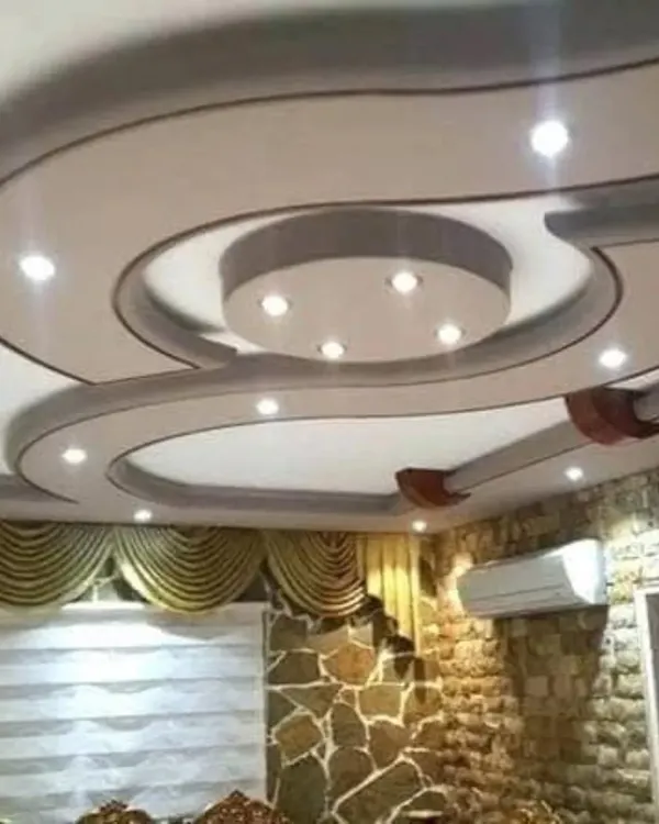 A finished gypsum false ceiling featuring a smooth, curved design with perfectly placed recessed spotlights. This type of design adds a soft, modern flow to a living or dining area.