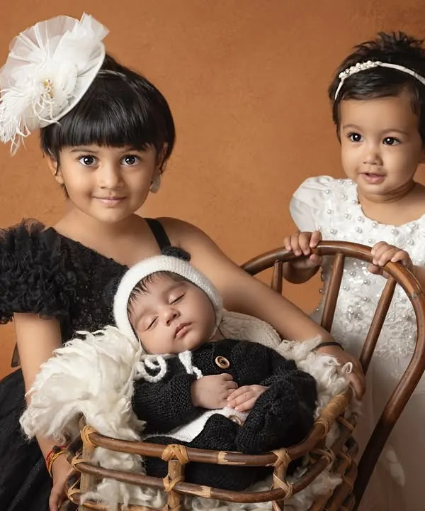 A perfect portrait of sibling love. Two older sisters gently watch over their newborn brother, who is nestled comfortably in a basket.