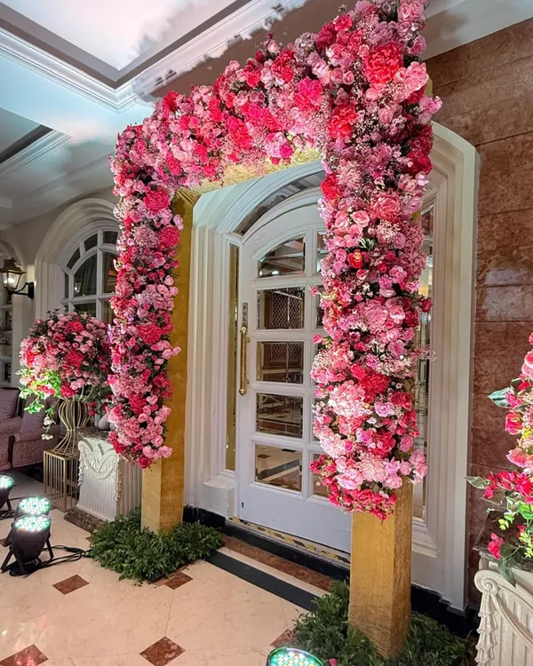 A magnificent floral arch made entirely of pink and red blooms frames a doorway, creating a stunning and romantic entrance for a Roka ceremony.
