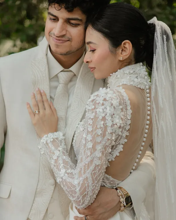 A tender moment between the bride and groom, showcasing the intricate details of the bride's high-neck, pearl-buttoned gown.